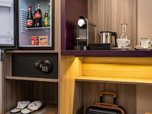 A compact hotel room with a minibar, a safe, a coffee maker, a kettle, and a suitcase. - Mercure Salzburg City (Salzburg)