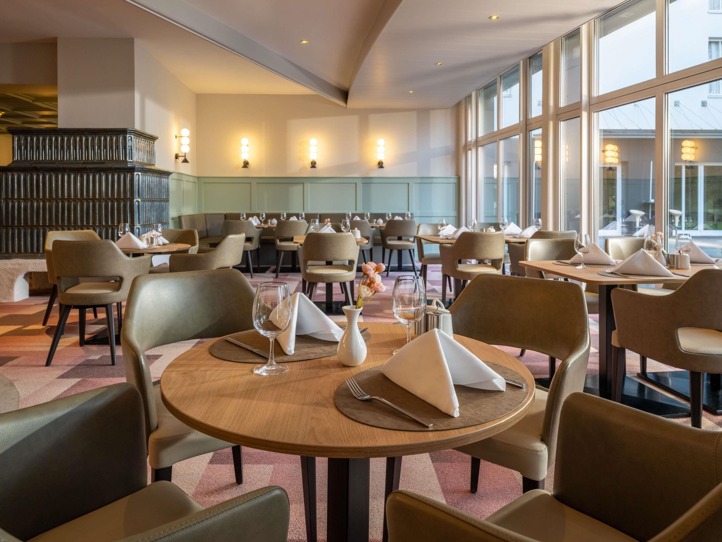Ein Restaurant mit runden Tischen, Stühlen und Blick durch große Fenster.