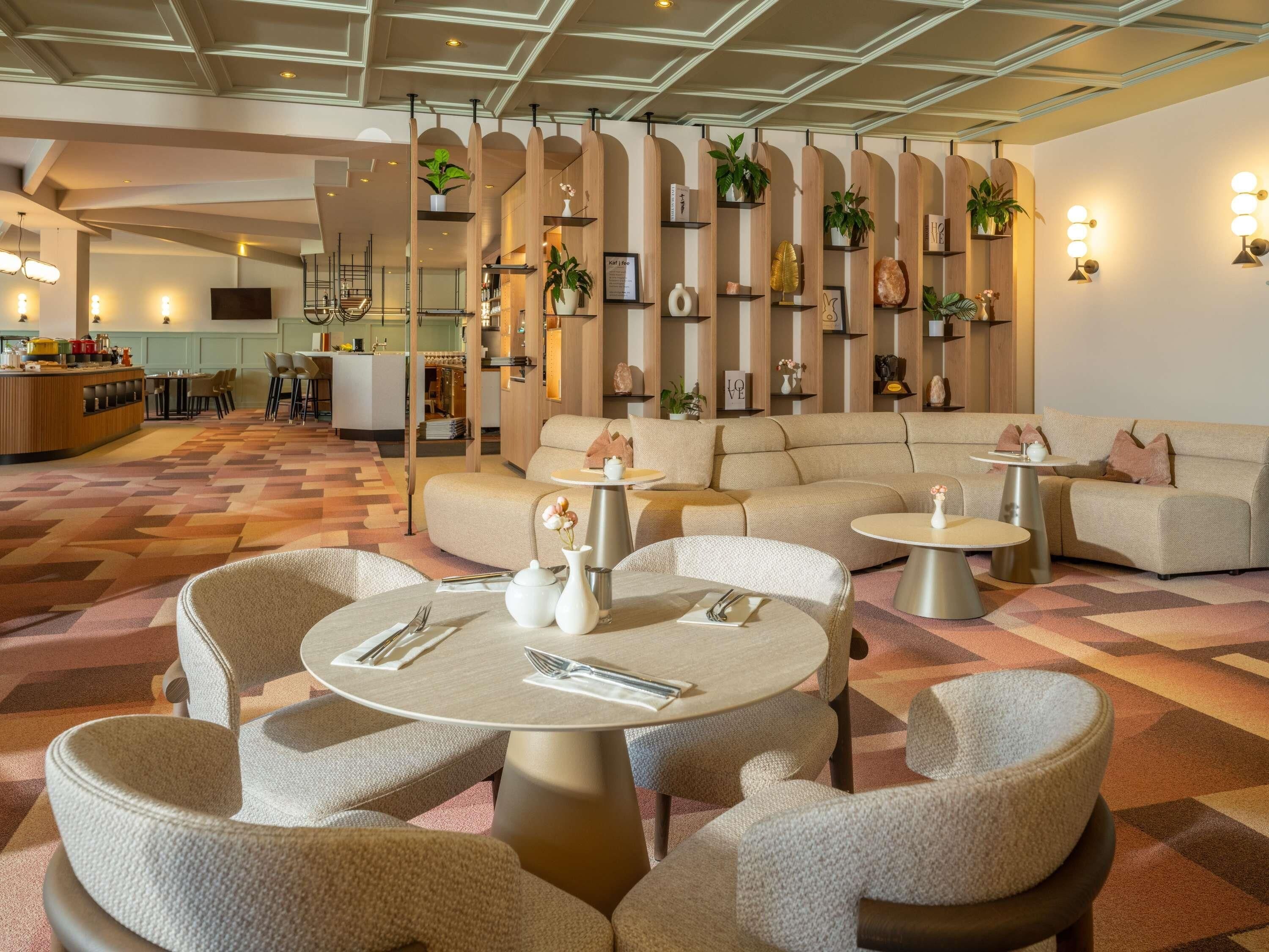 A modern hotel lobby with round tables, sofas, and a bar area.