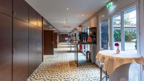 A hotel corridor with a patterned floor, a table with a vase, and a view through the window. - Mercure Salzburg City (Salzburg)