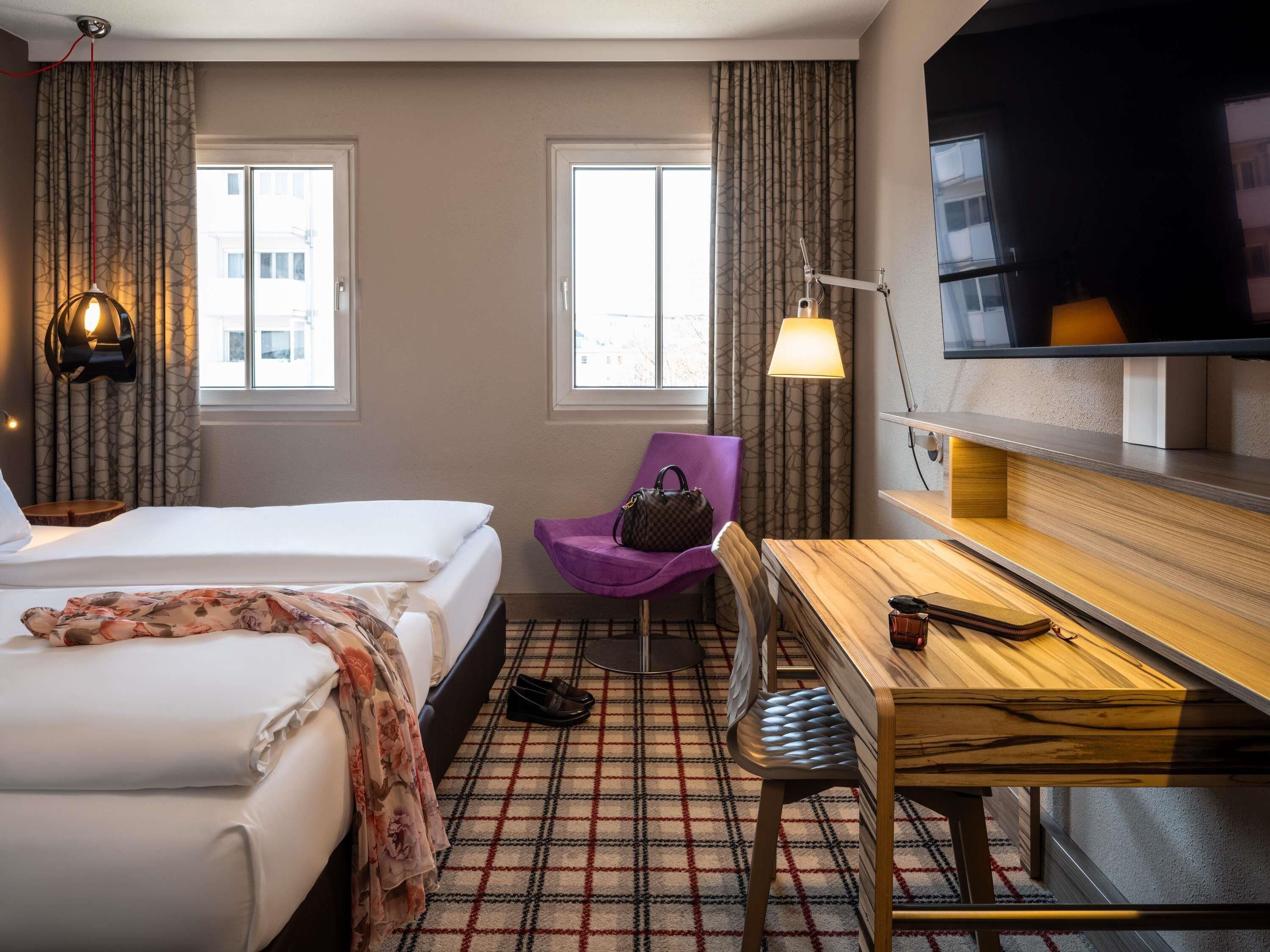Een hotelkamer met twee bedden, een bureau, een stoel, een televisie en een raam.