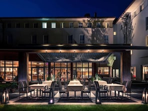 A covered outdoor dining area with tables and chairs, a building with multiple windows, and a clear sky. - Mercure Salzburg City (Salzburg)