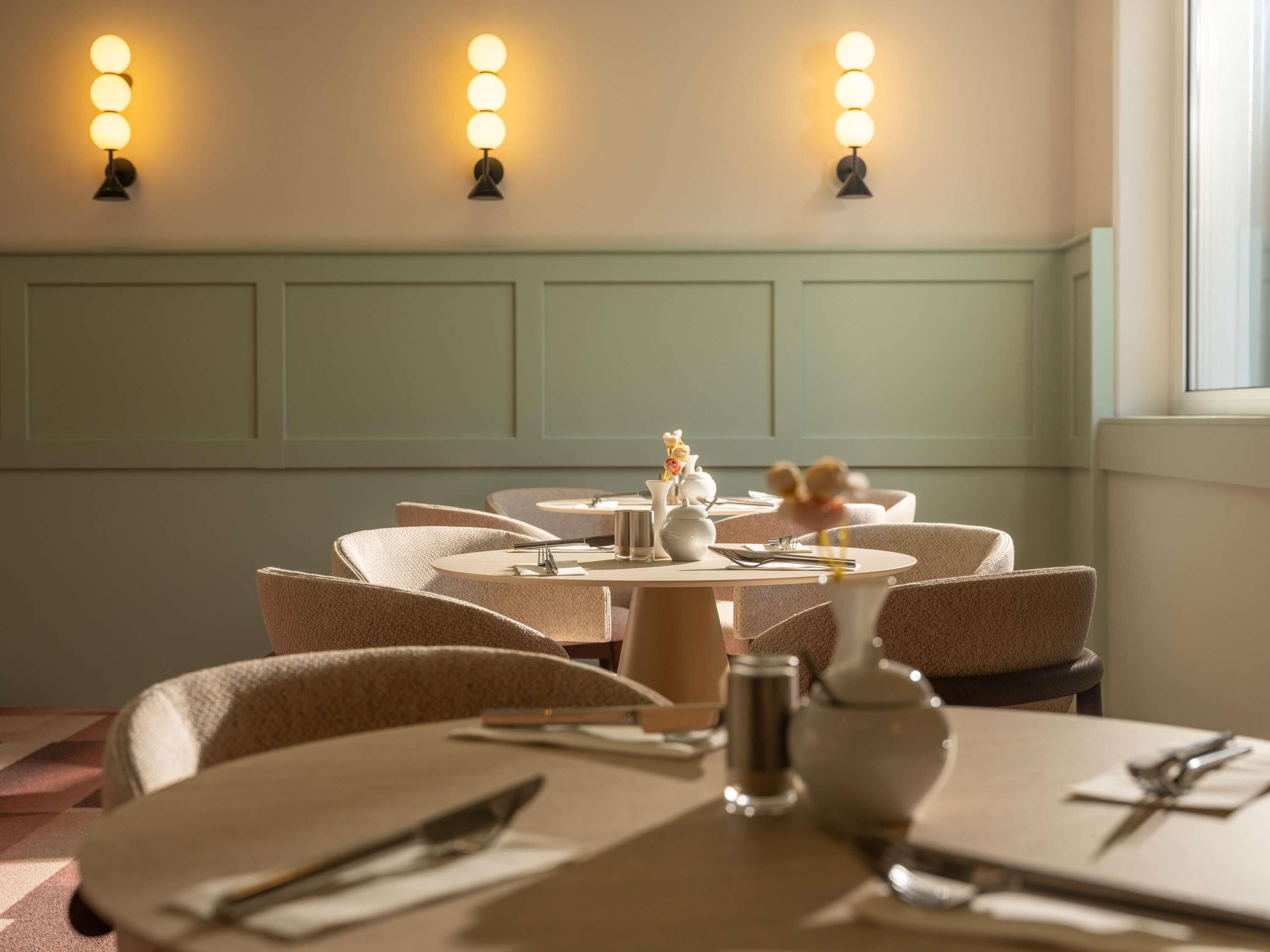 A dining area with round tables, chairs, and wall-mounted lights.