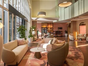 Eine geräumige Lobby mit modernen Möbeln, großen Fenstern und einer zentralen Sitzgruppe.