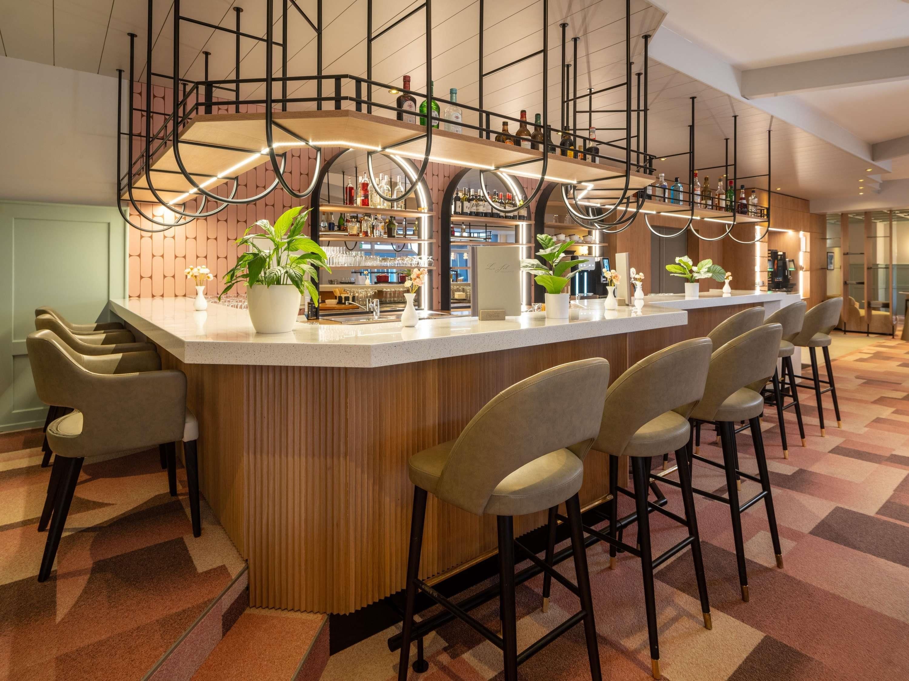 Zona de bar moderna con mostrador curvo, taburetes y plantas en macetas.