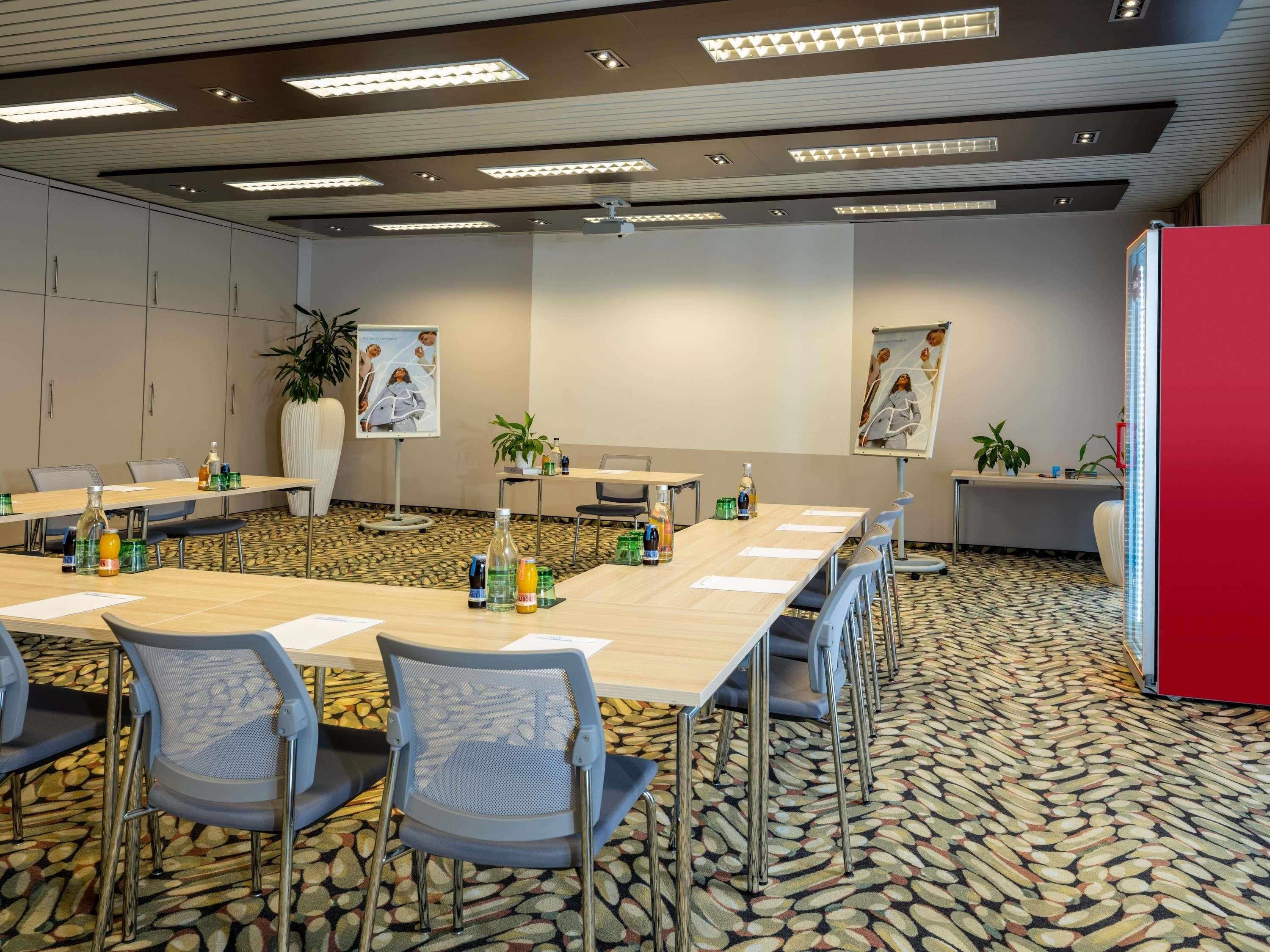 A conference room with a long table, chairs, a projector screen, and a red accent wall.