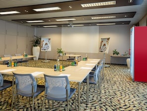 Ein Konferenzraum mit einem langen Tisch, Stühlen, einer Projektionsleinwand und einer roten Akzentwand.