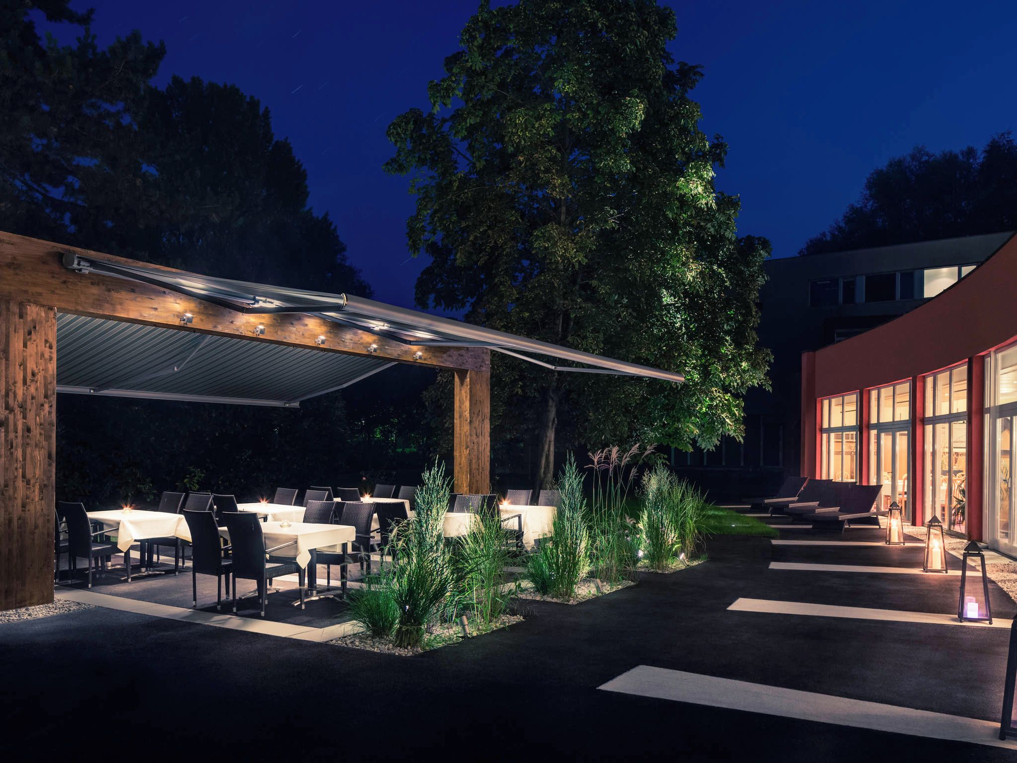 An outdoor dining area with tables and chairs, a covered seating area, and a building with large windows.