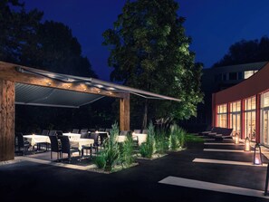 An outdoor dining area with tables and chairs, a covered seating area, and a building with large windows. - Mercure Salzburg City (Salzburg)