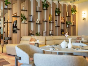 A modern interior with a sofa, round tables, and shelves with plants and decorative items. - Mercure Salzburg City (Salzburg)