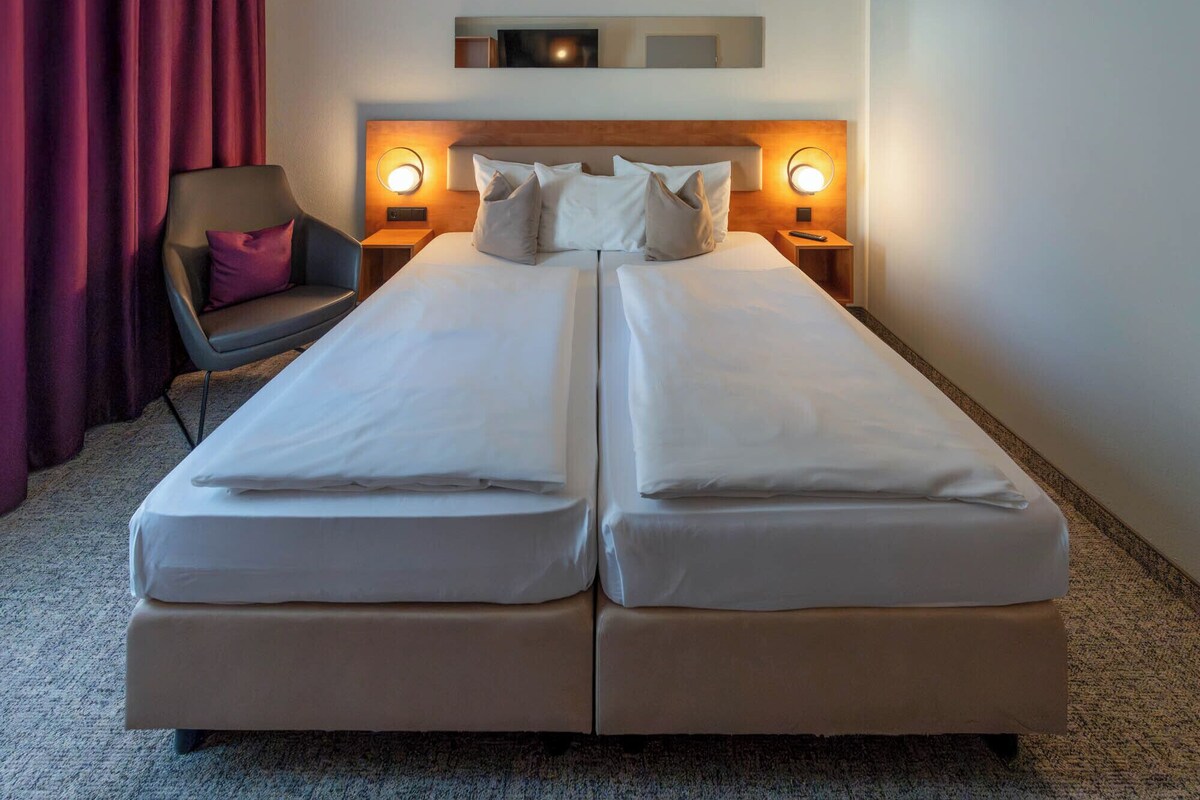 A double bed with two pillows, a chair, and bedside lamps in a hotel room.