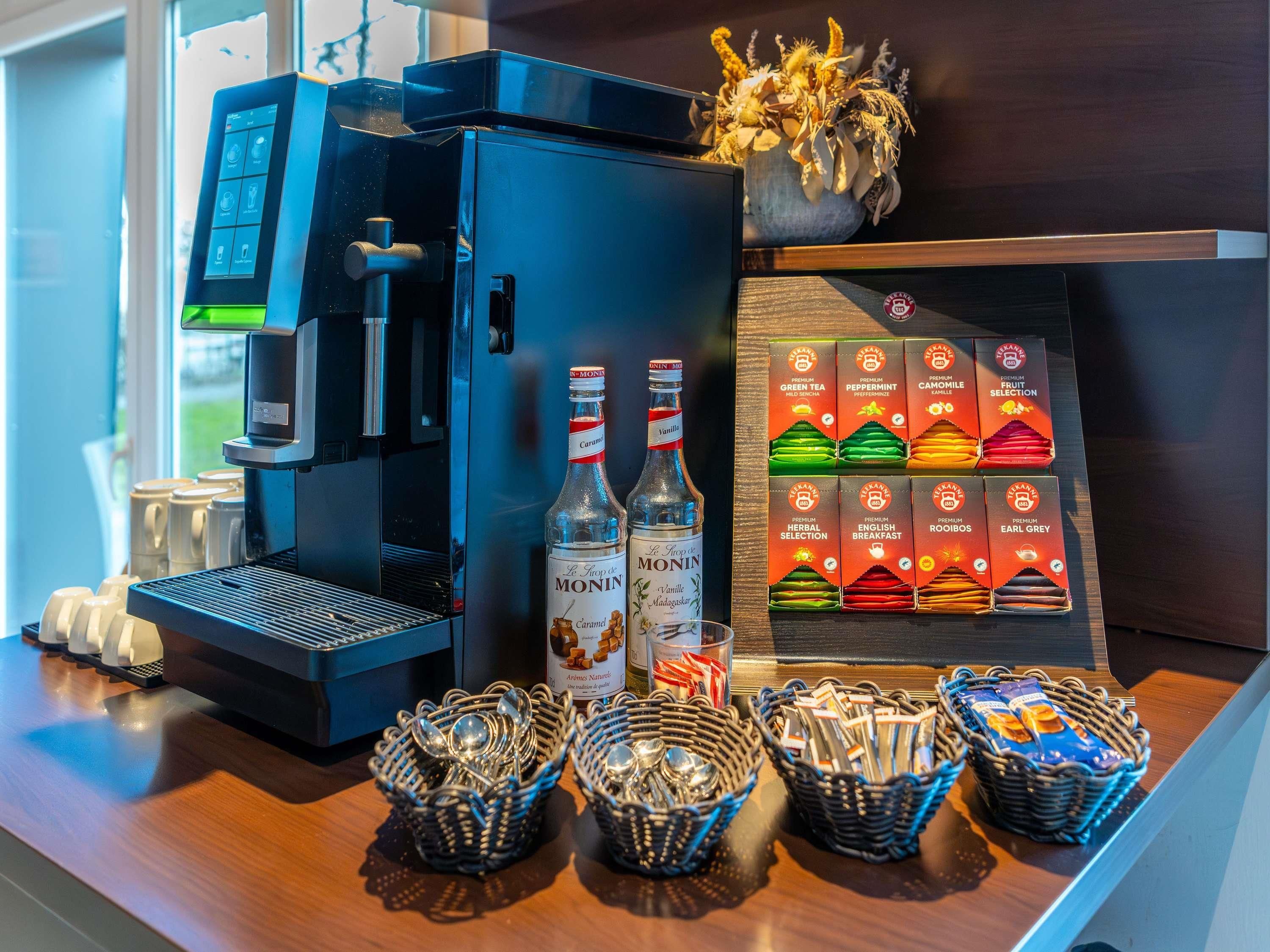 A coffee machine, two bottles of Monin syrup, and a display of Monin tea boxes.