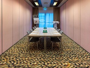 A conference room with a long table, chairs, a patterned carpet, and a view of the outdoors through large windows.