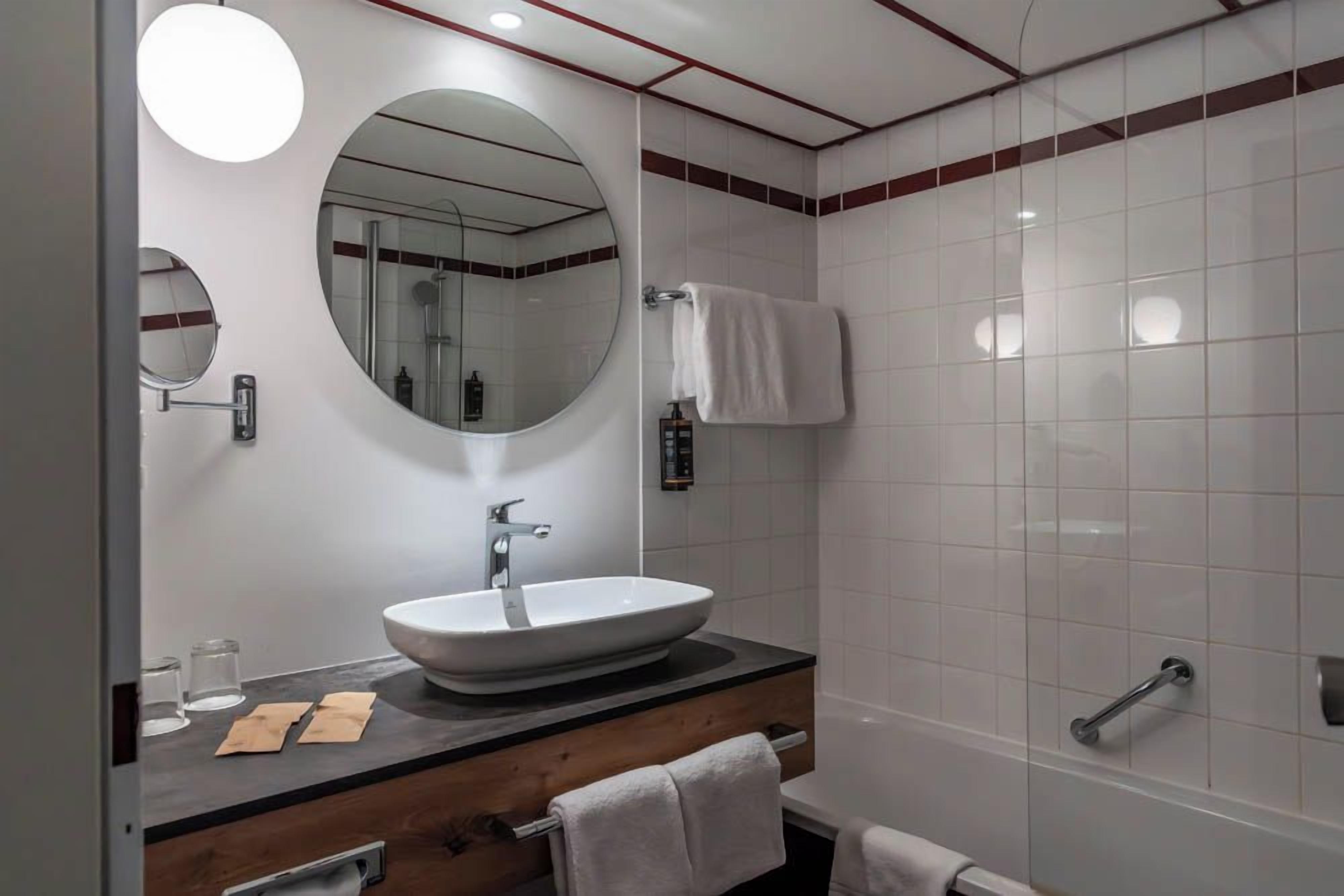 Un bagno moderno con uno specchio rotondo, un lavabo a incasso e una vasca da bagno.