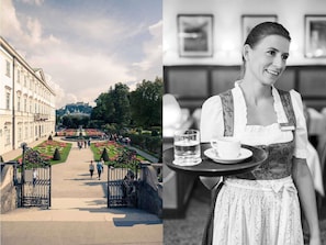 A historical building with a garden pathway and a person serving a tray with a glass of water and a cup.