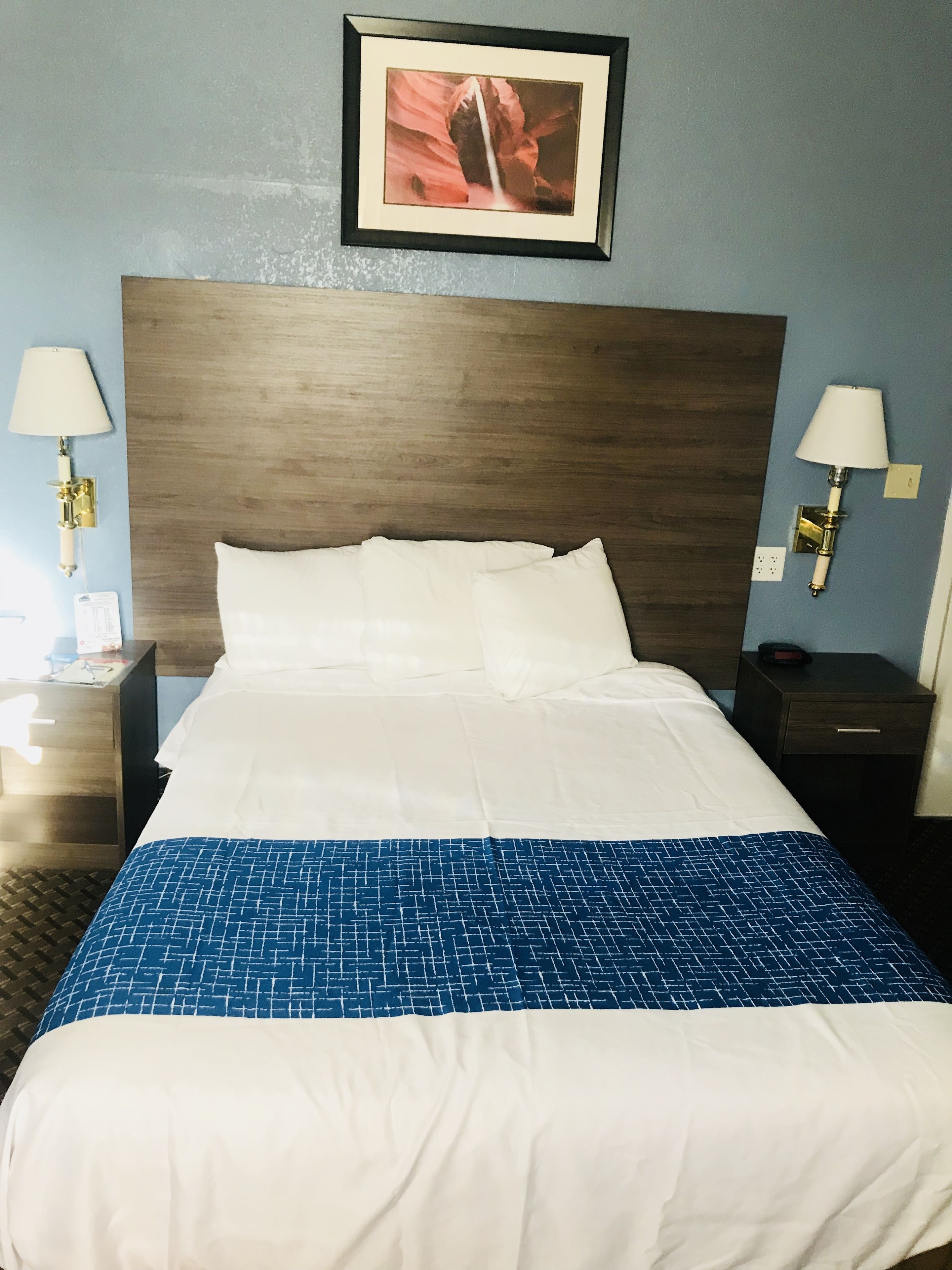 A neatly made bed with a blue and white patterned bedspread, two bedside lamps, and a framed picture above the headboard.