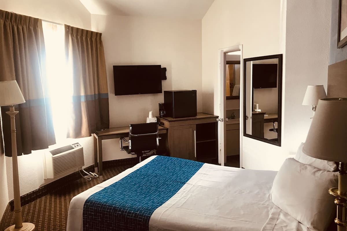 Ein Hotelzimmer mit Bett, Schreibtisch, Sessel, Fernseher und Spiegel.