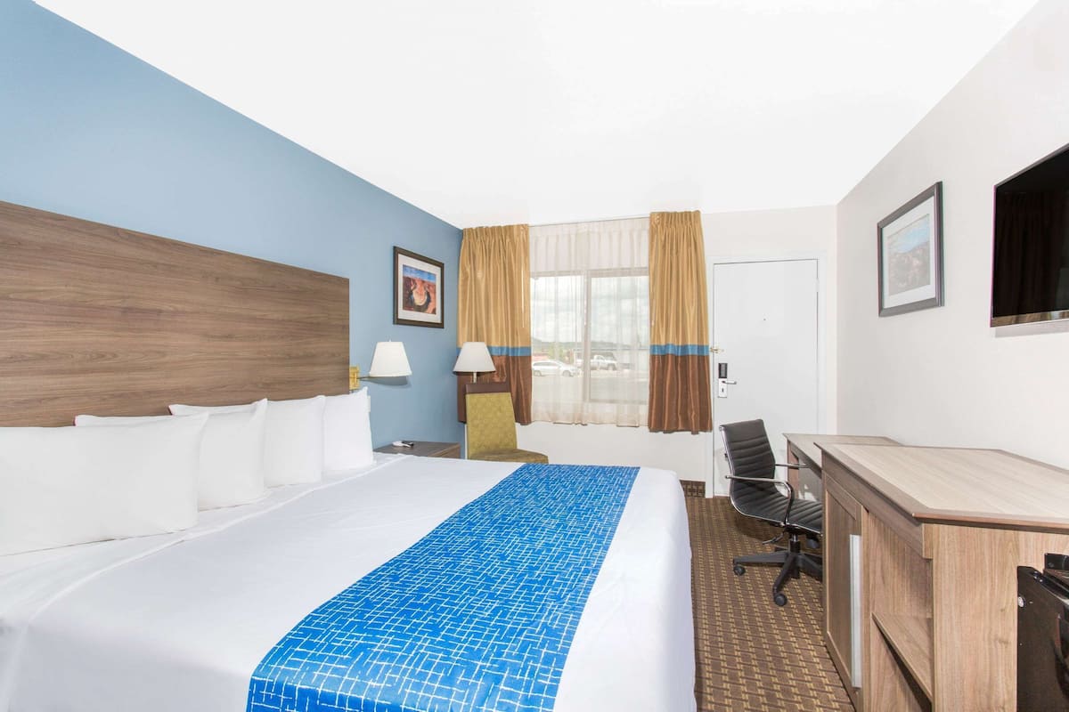 Ein Hotelzimmer mit Bett, Schreibtisch, Stuhl und einem Fenster mit Vorhängen.