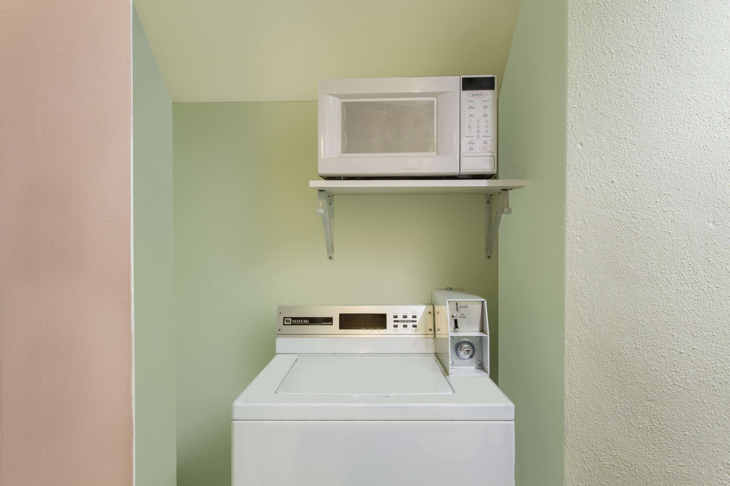 A compact laundry room with a washing machine and a microwave on a shelf.