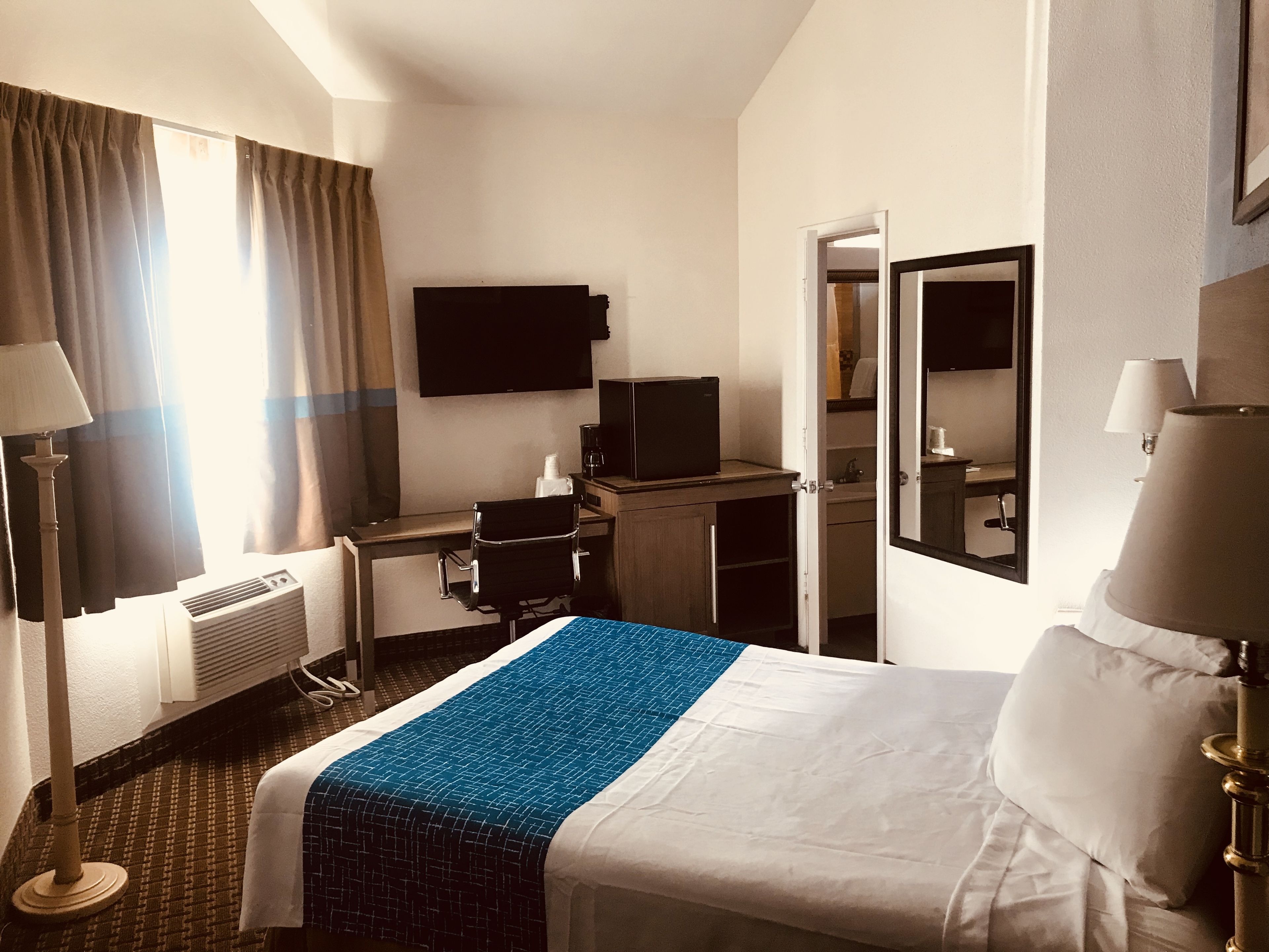 A hotel room with a bed, desk, chair, television, and a bathroom visible through an open door.