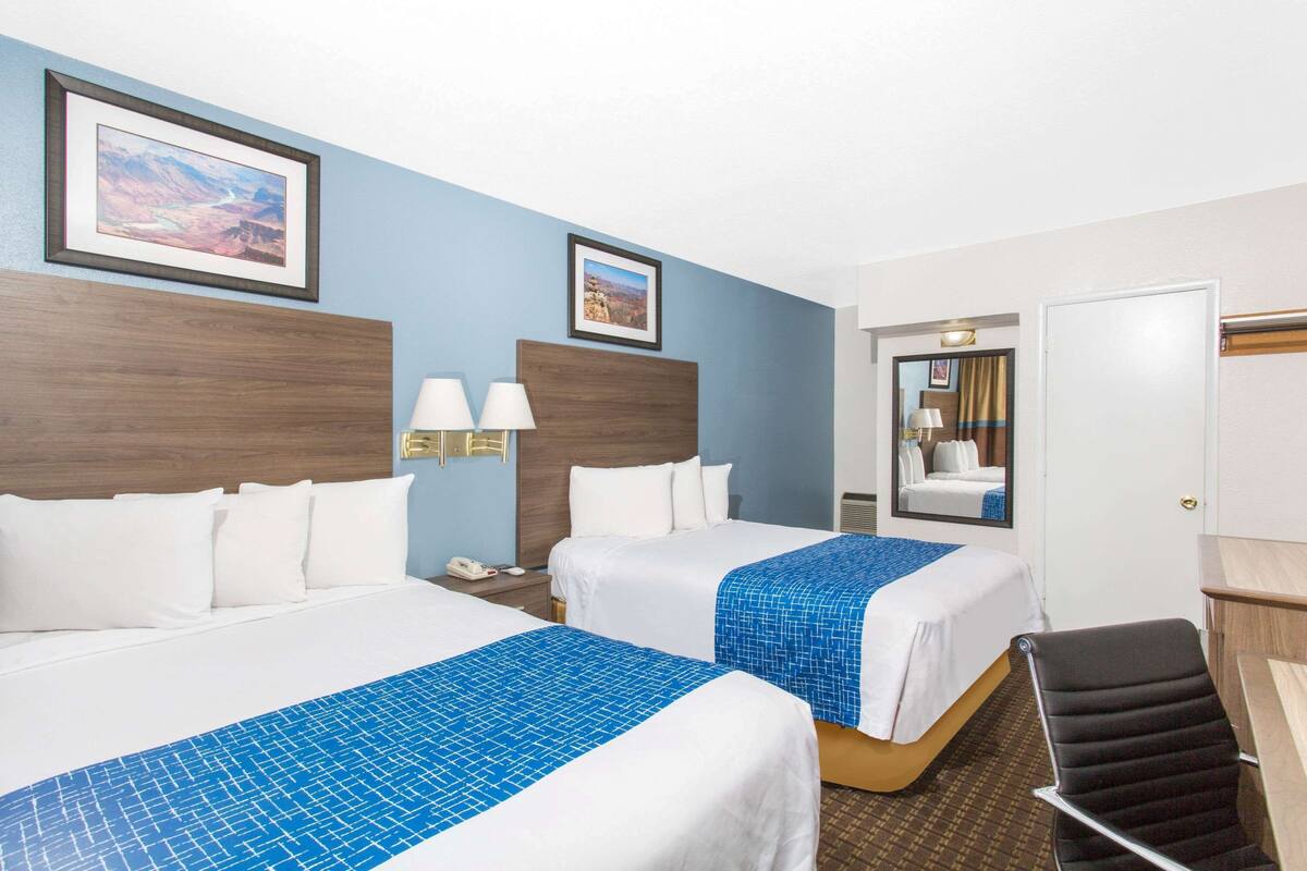 Ein Hotelzimmer mit zwei Betten, einem Schreibtisch, einem Stuhl und einem Spiegel.