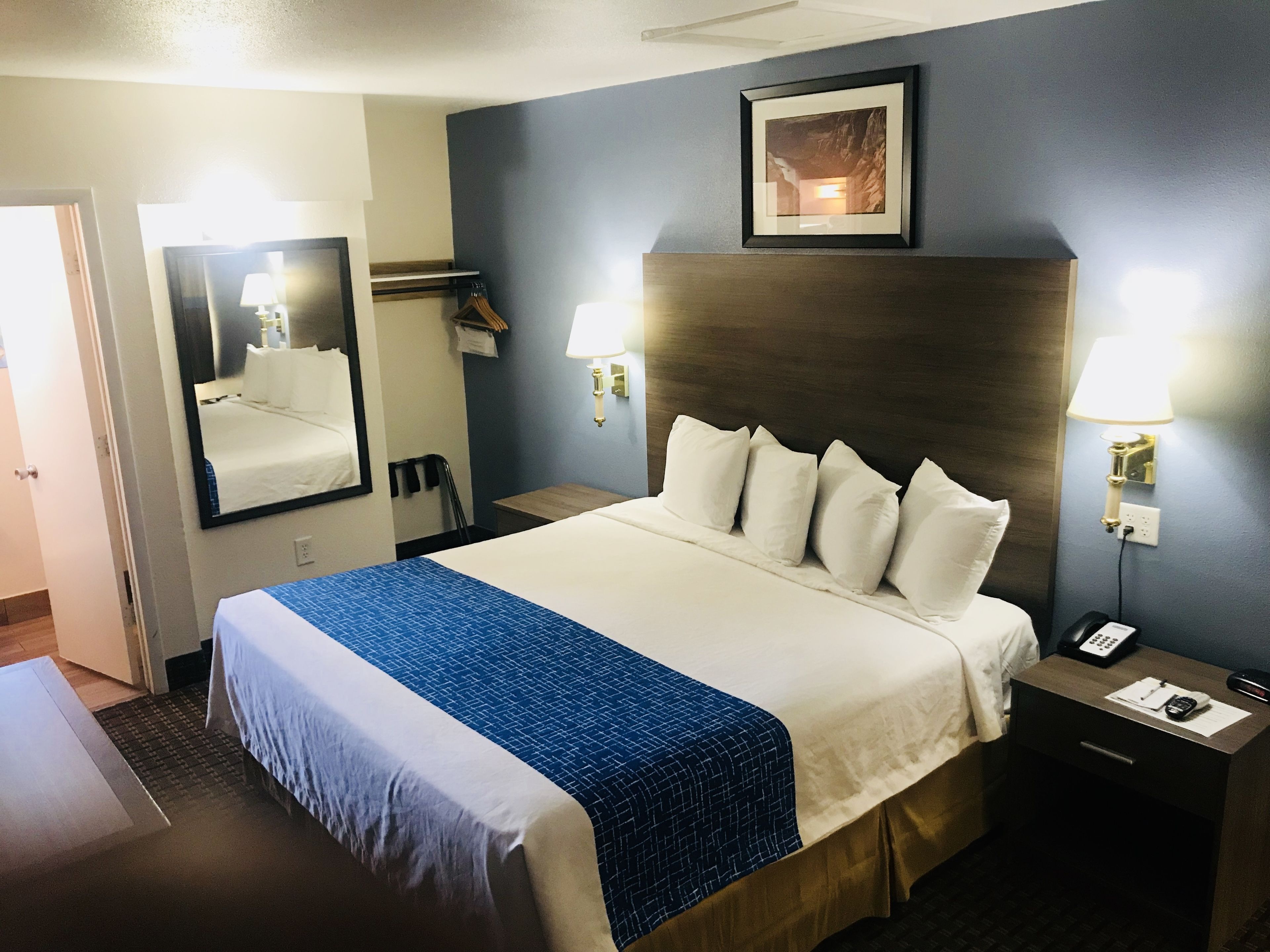 A hotel room with a large bed, a headboard, two bedside tables, a mirror, a framed picture on the wall, and a door.