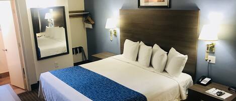 A hotel room with a large bed, a headboard, two bedside tables, a mirror, a framed picture on the wall, and a door.