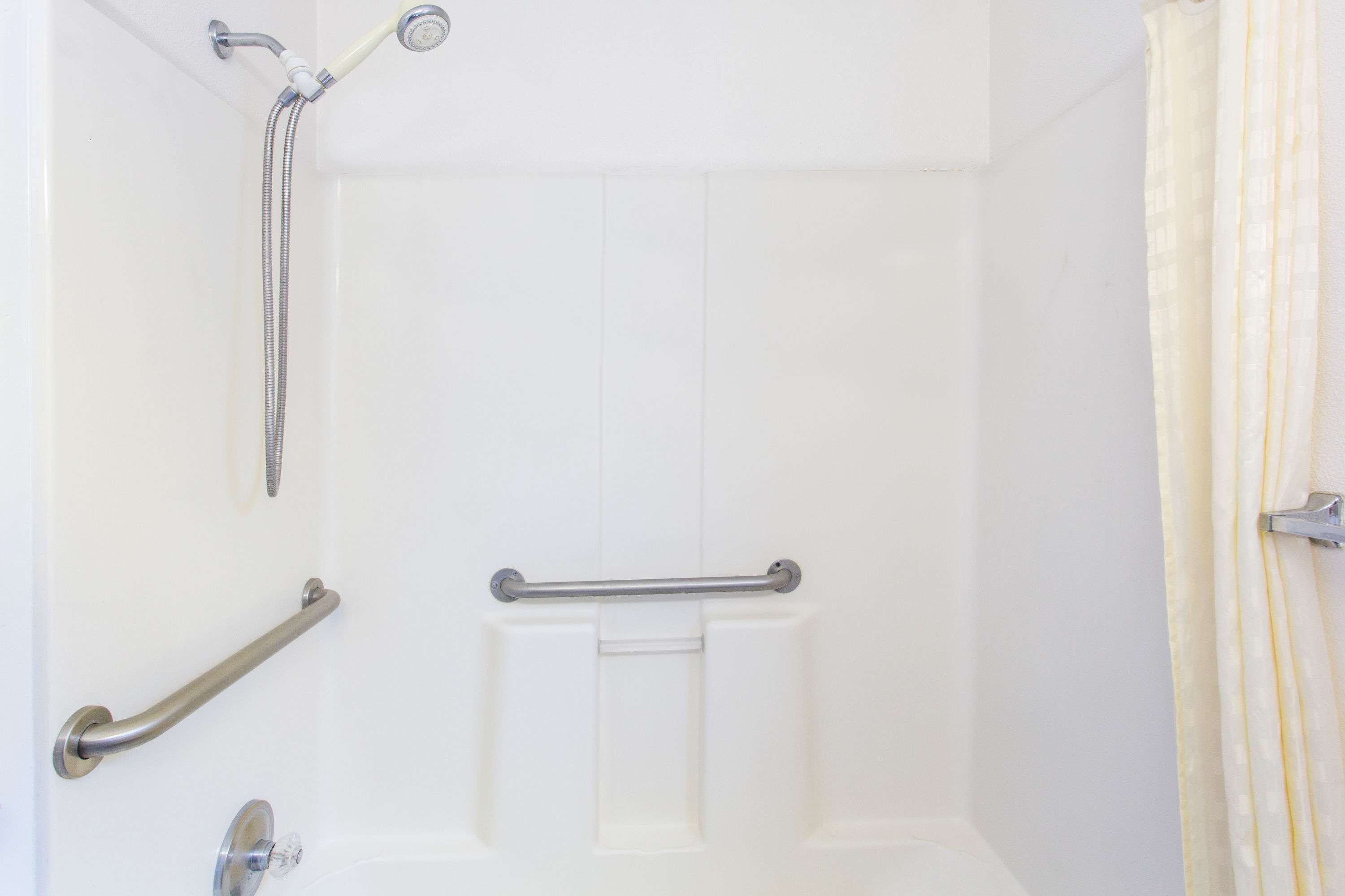 A bathroom with a shower, grab bars, and a toilet.