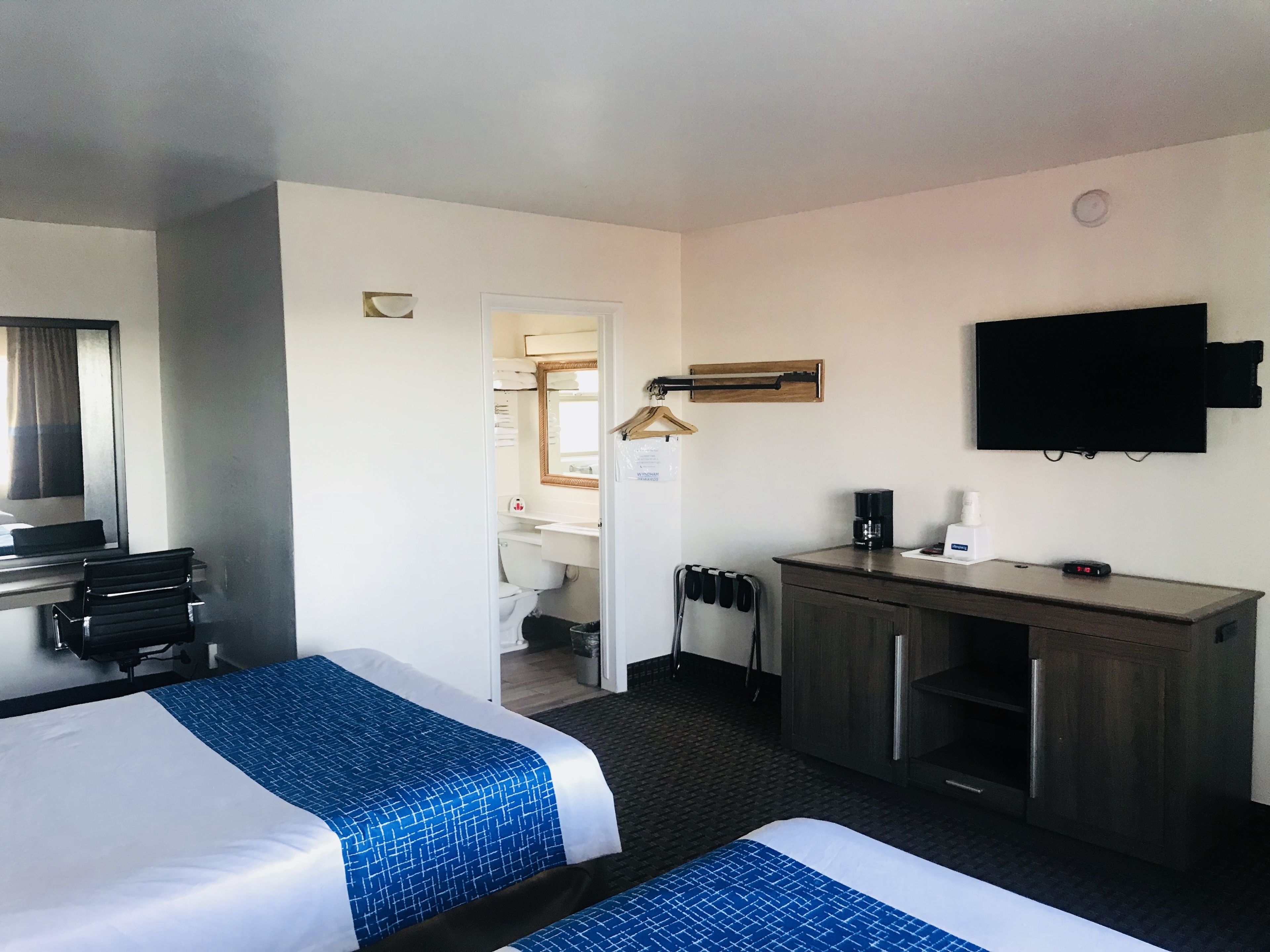 A hotel room with two beds, a desk, a TV, and a bathroom visible through an open door.
