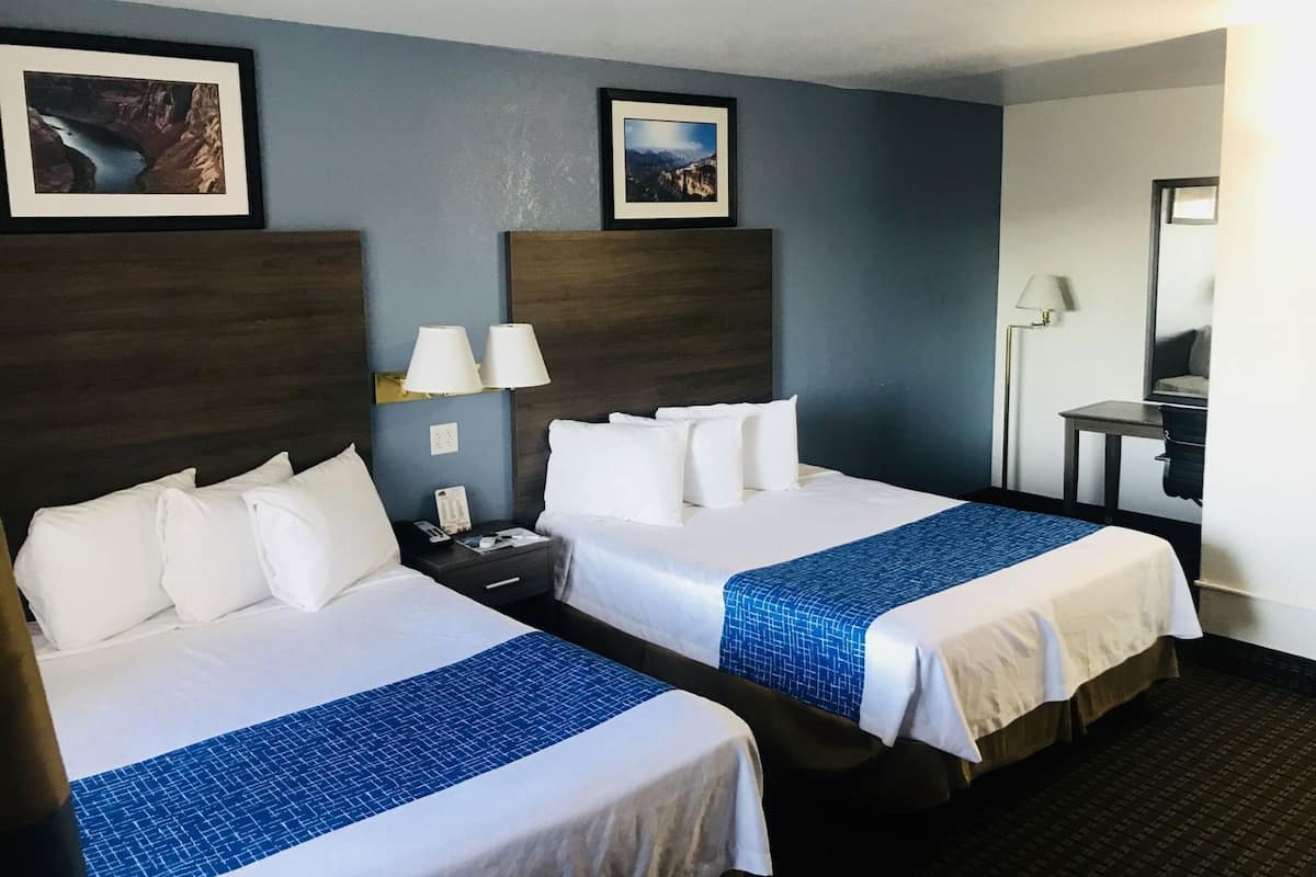 Ein Hotelzimmer mit zwei Betten, einem Schreibtisch, einem Sessel, einer Lampe und zwei gerahmten Bildern an der Wand.
