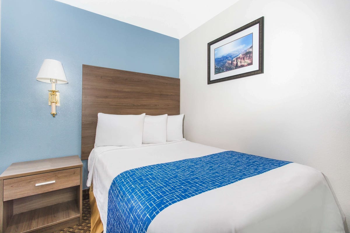 Ein Hotelzimmer mit Bett, Nachttisch, Lampe und einem gerahmten Bild an der Wand.