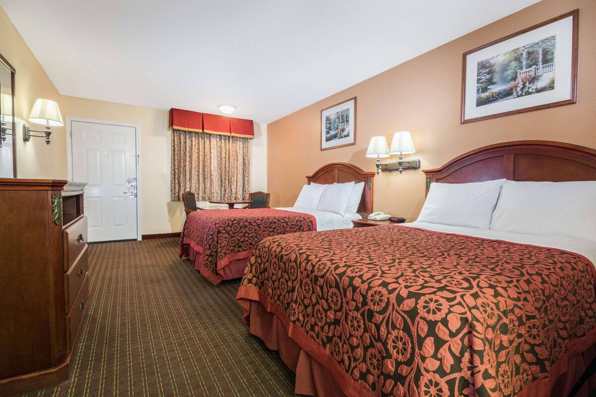 A hotel room with two beds, a desk, a chair, a wardrobe, and a door.