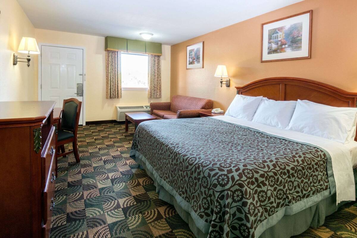 A hotel room with a bed, a desk, a chair, a sofa, and two wall-mounted lamps.