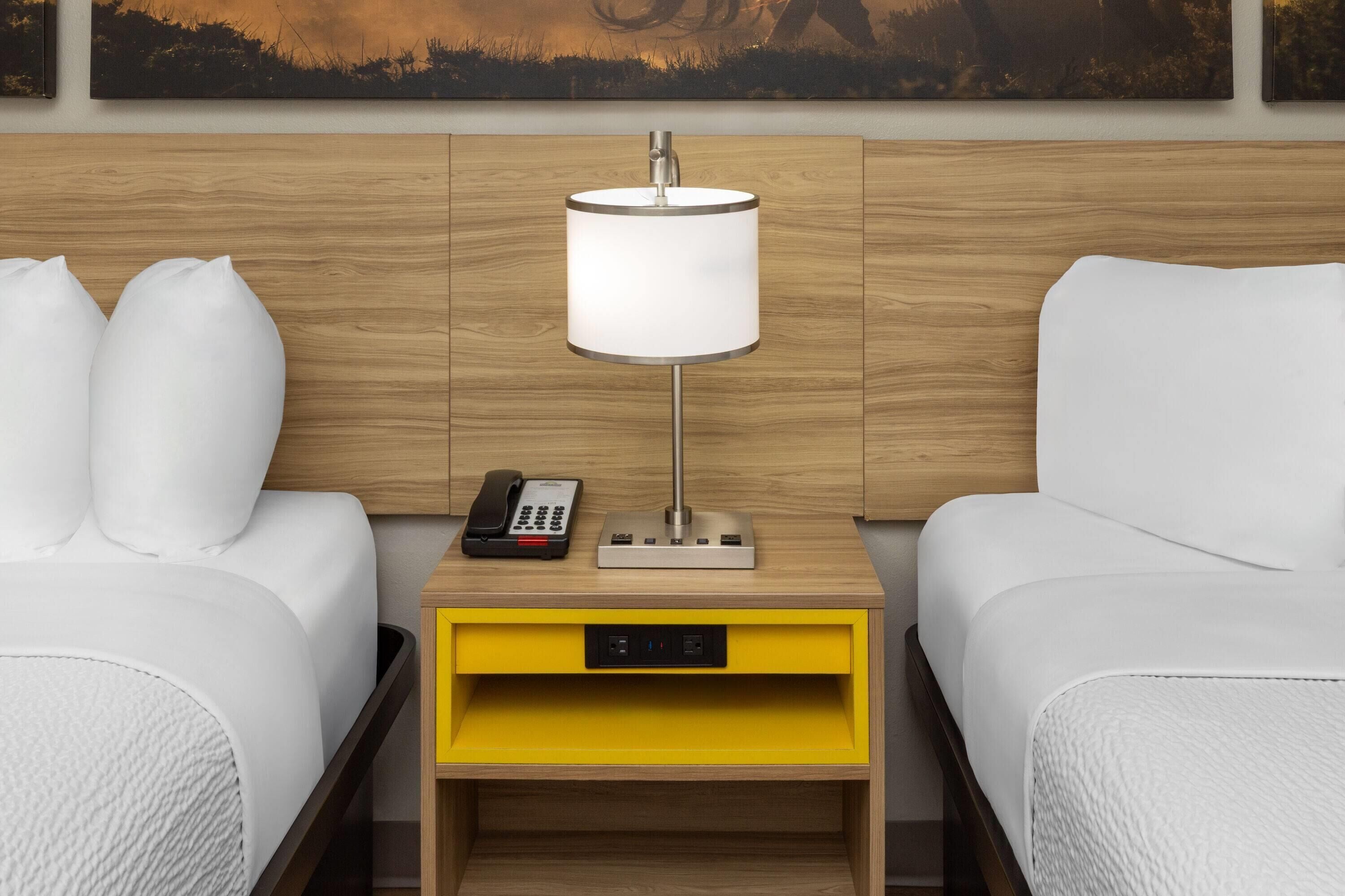 Habitación de hotel con dos camas, una mesita de noche con lámpara, teléfono y toma de corriente.