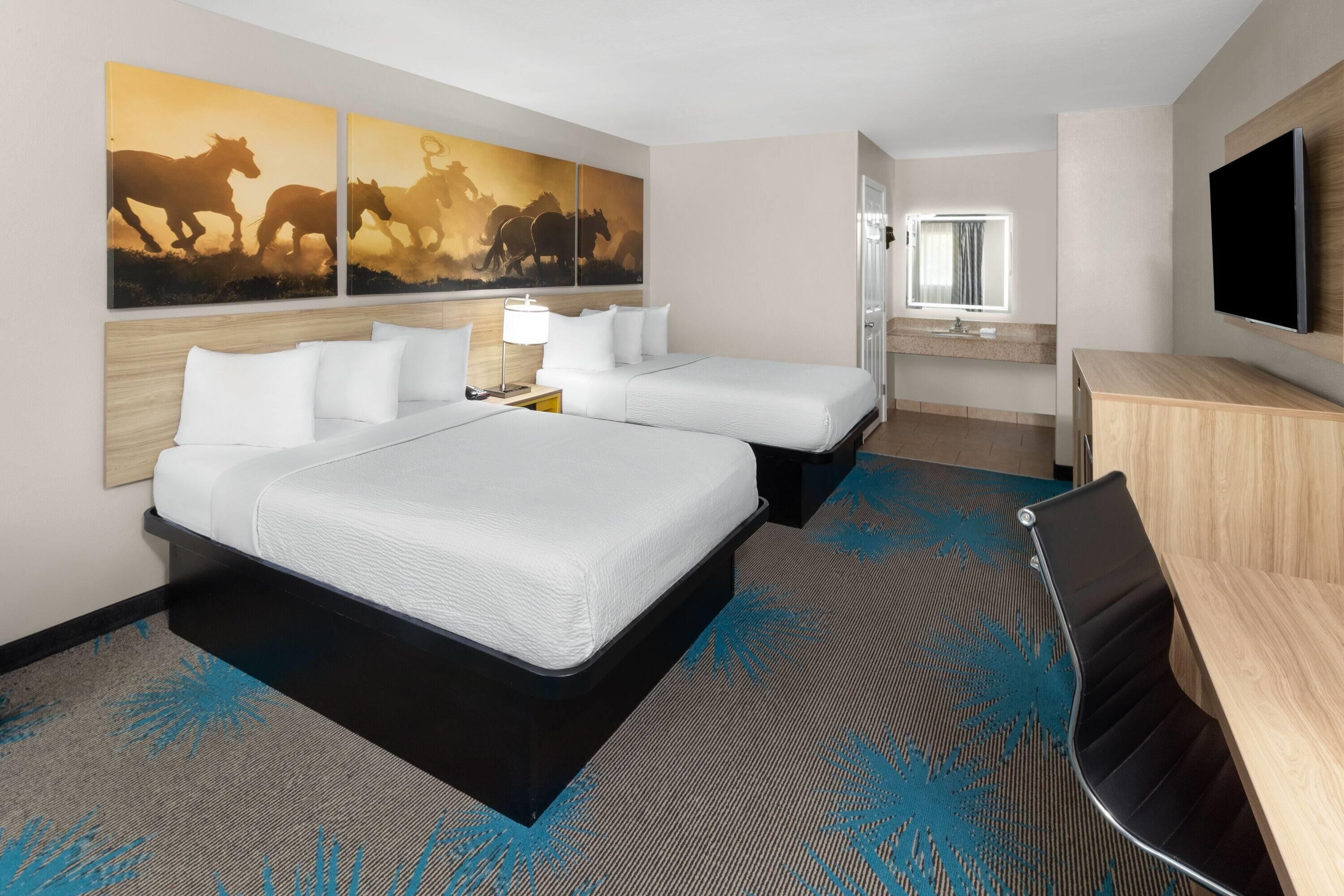 Une chambre d’hôtel avec deux lits, un bureau, une télévision et des œuvres d’art accrochées au mur.