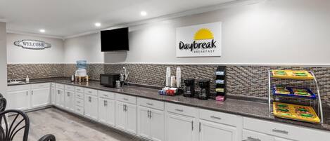 A hotel kitchen with a 'Daybreak Breakfast' sign, a welcome sign, and a water dispenser.