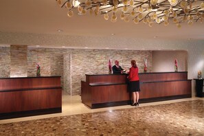 Un espace d’accueil comprenant un comptoir de réception en bois, un réceptionniste et un visiteur.