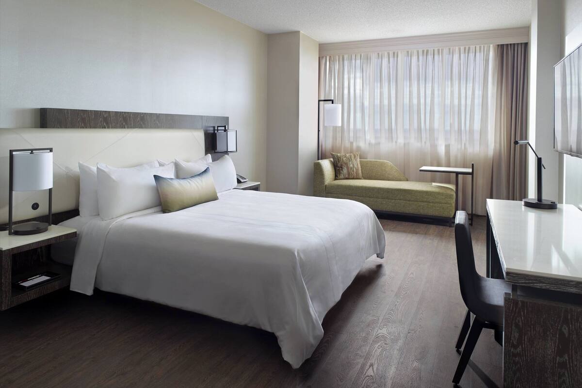 Una habitación de hotel con una cama grande, un escritorio, una silla, un sofá y un televisor.