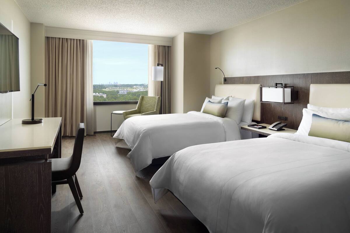 Habitación de hotel con dos camas, un escritorio, una silla, un televisor y una ventana con vista a la ciudad.