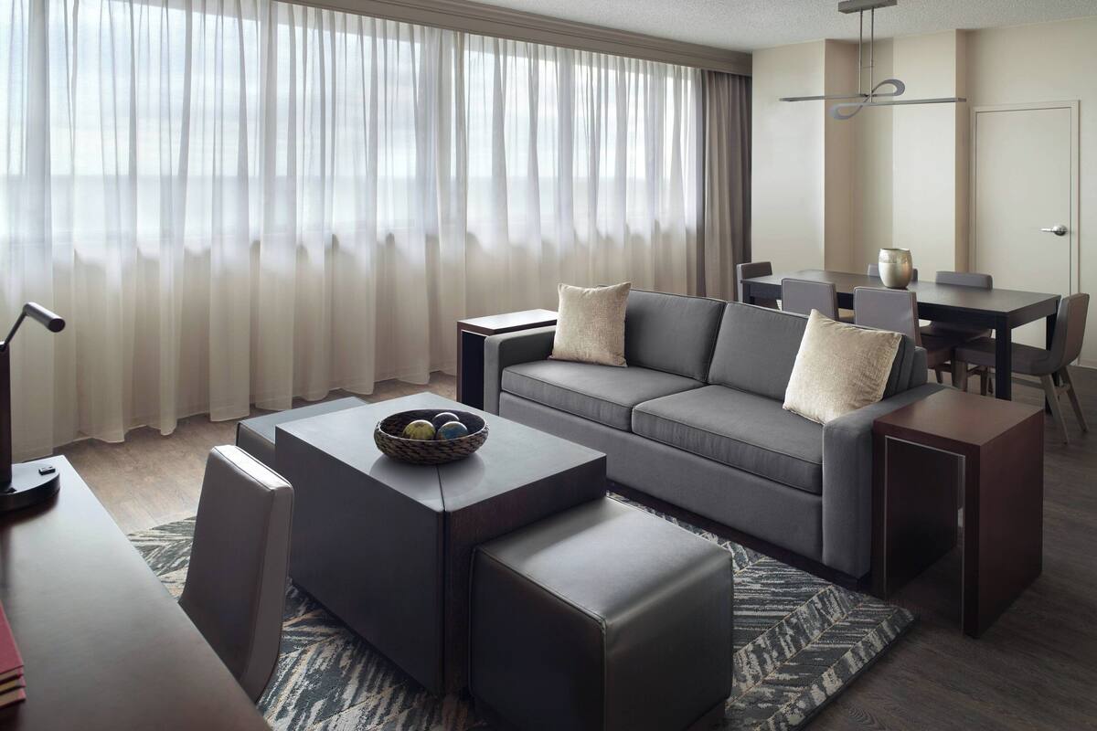 Una sala de estar moderna con un sofá gris, una mesa de centro y un comedor con una mesa y sillas.