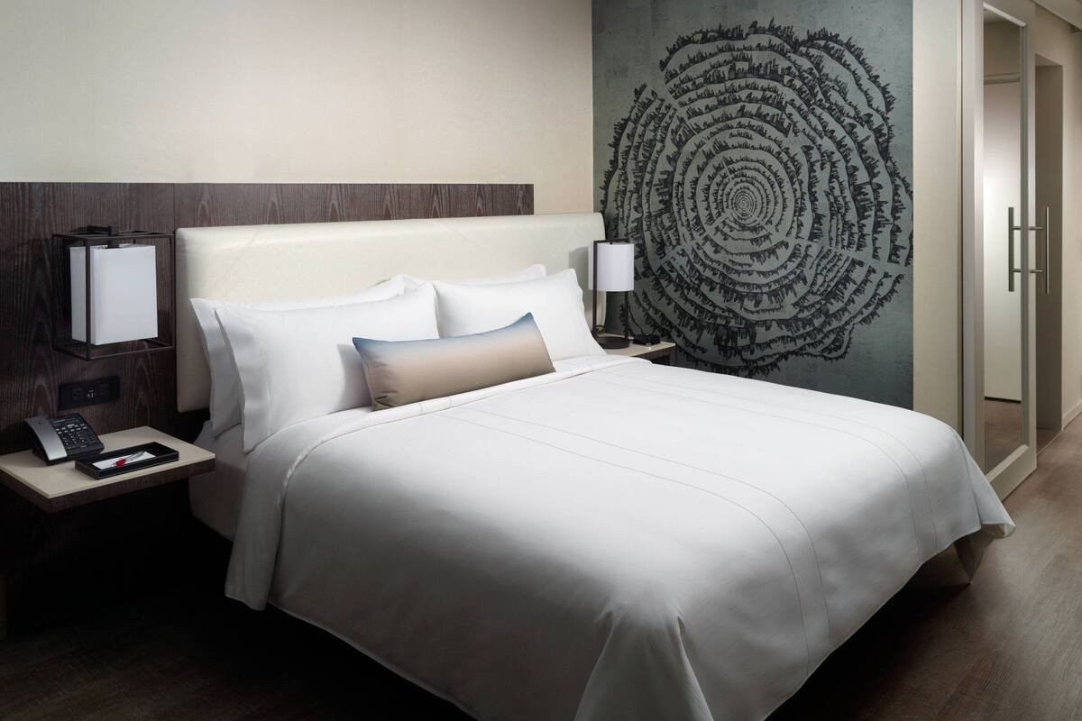 Una habitación de hotel con una cama grande, una mesita de noche con un teléfono y una lámpara, y una pared con un diseño circular.