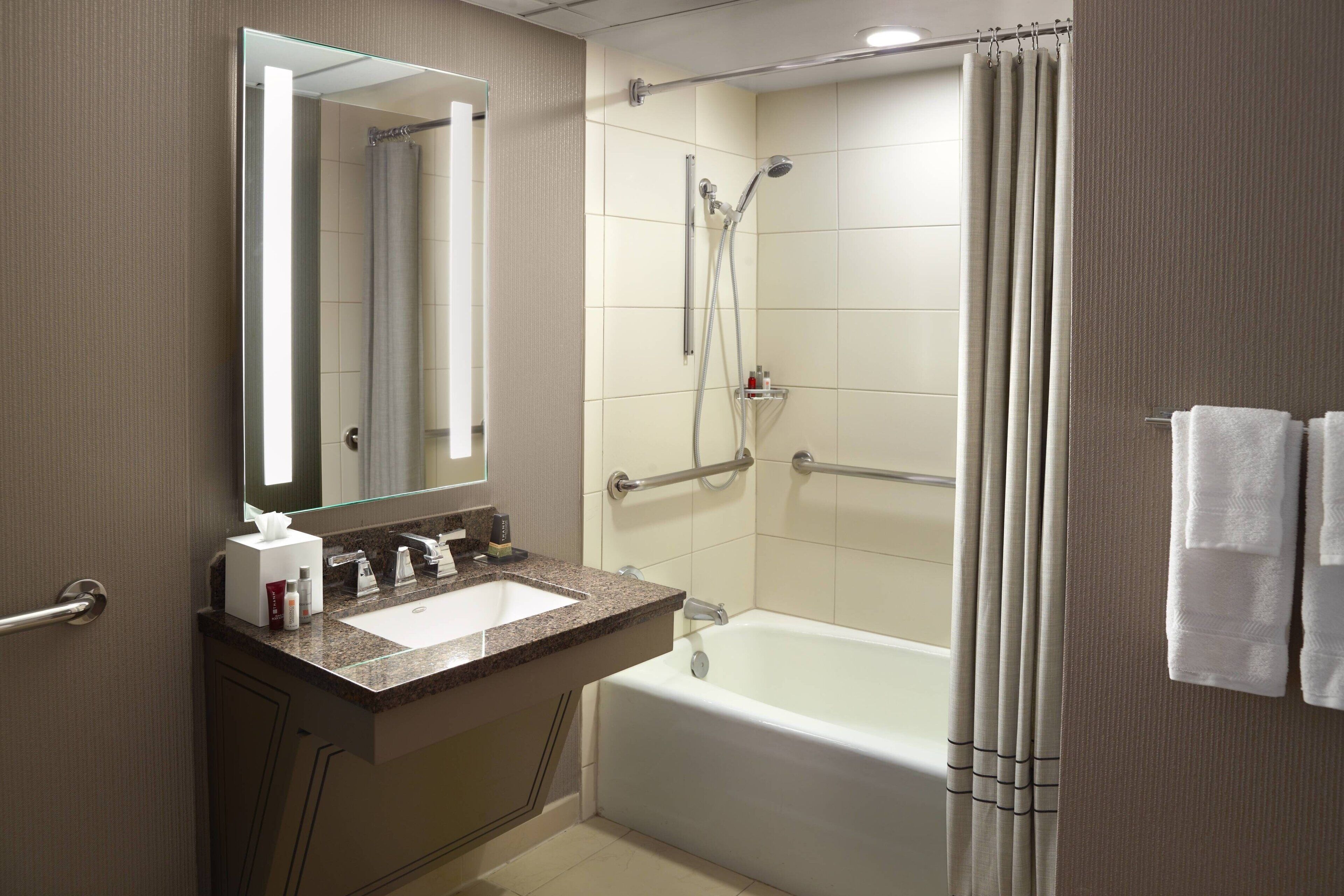 A modern bathroom with a sink, mirror, shower, and bathtub.