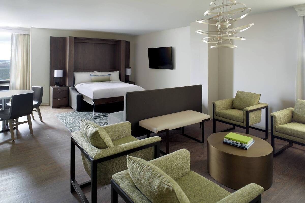 Habitación de hotel con cama, escritorio, dos sillones, un banco y una mesa de centro redonda.
