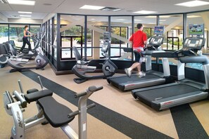 Une salle de sport équipée de tapis de course, d’appareils de musculation et dotée d’une grande fenêtre donnant sur une piscine.