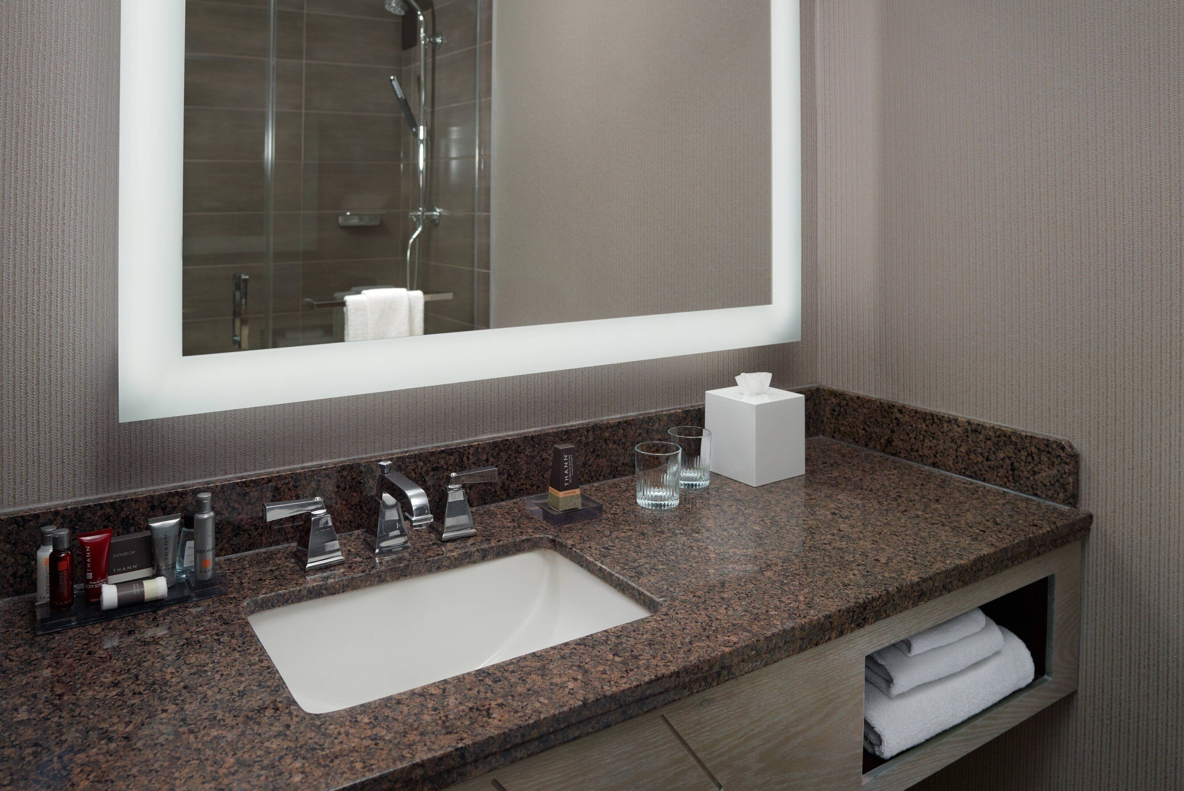 A bathroom with a granite countertop, a white sink, a large mirror, and a towel rack.