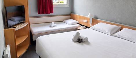 A hotel room with a bed, a TV, a desk, and a window with red curtains.