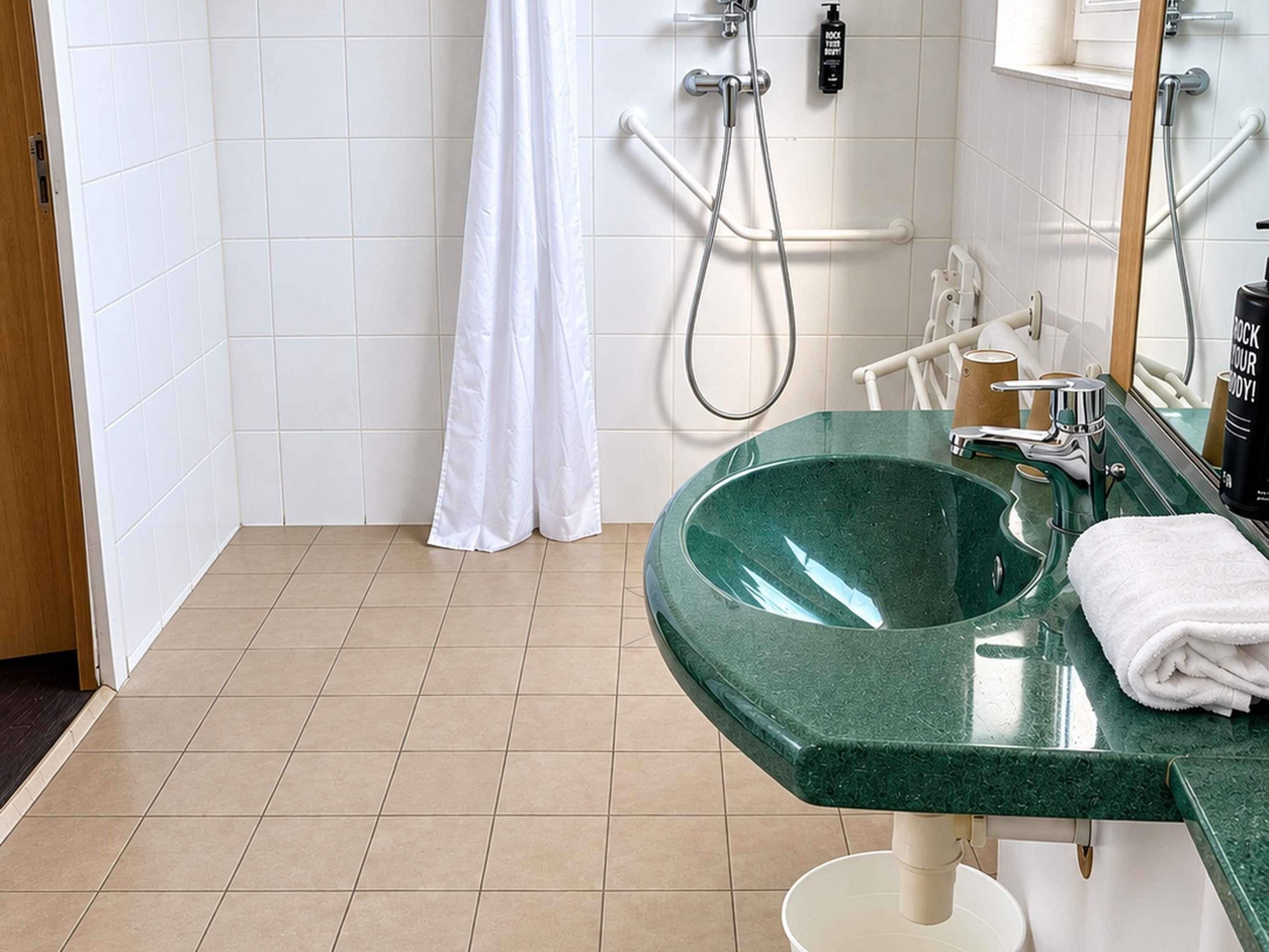 A bathroom with a green sink, white tiles, a shower, and a towel on the counter.