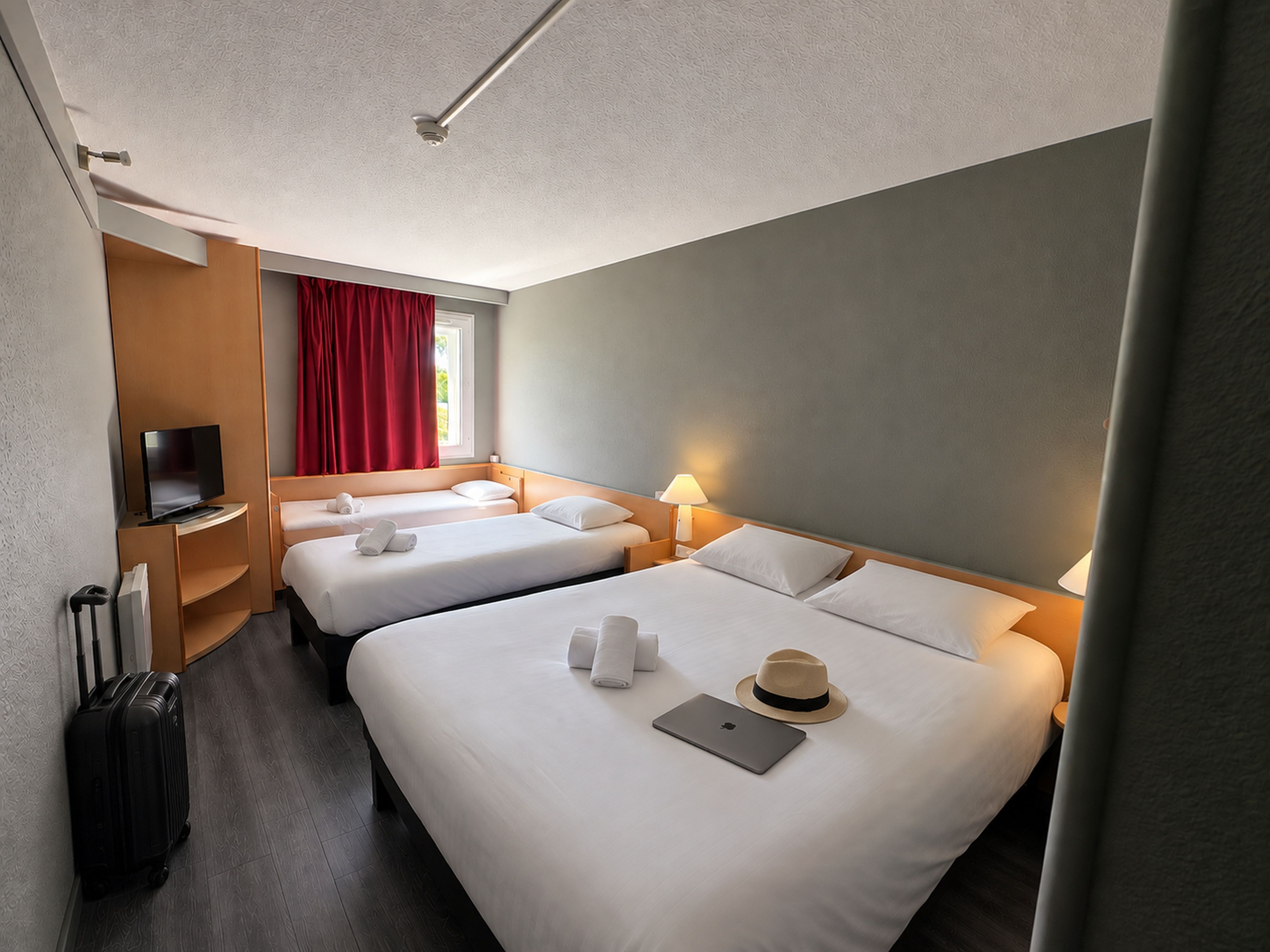 A hotel room with two beds, a television, a suitcase, and a laptop.