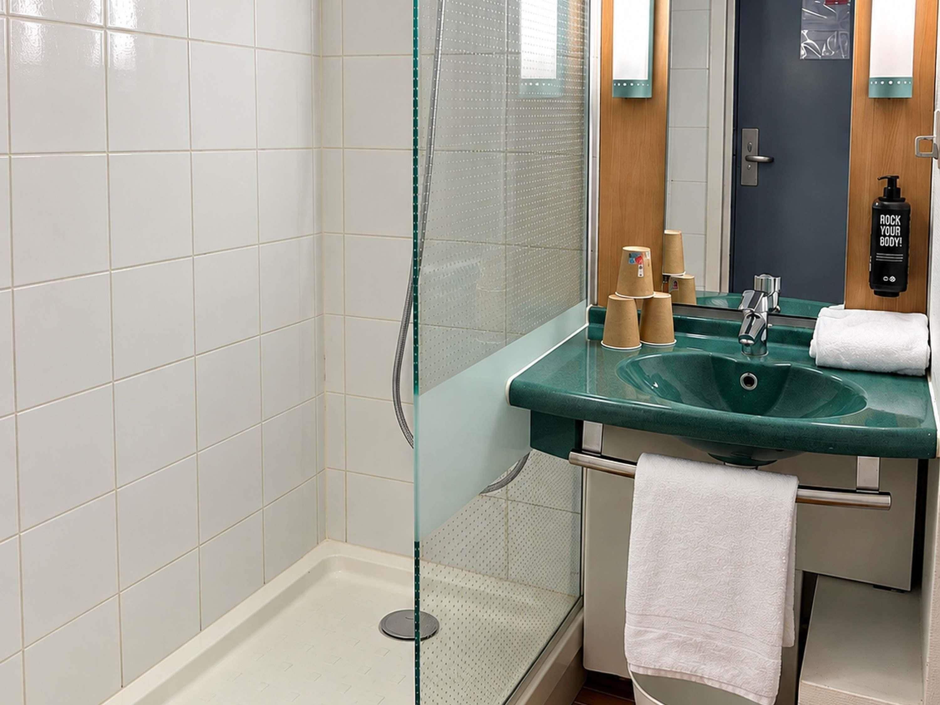 Un baño moderno con cabina de ducha de vidrio, un lavabo verde y un espejo.