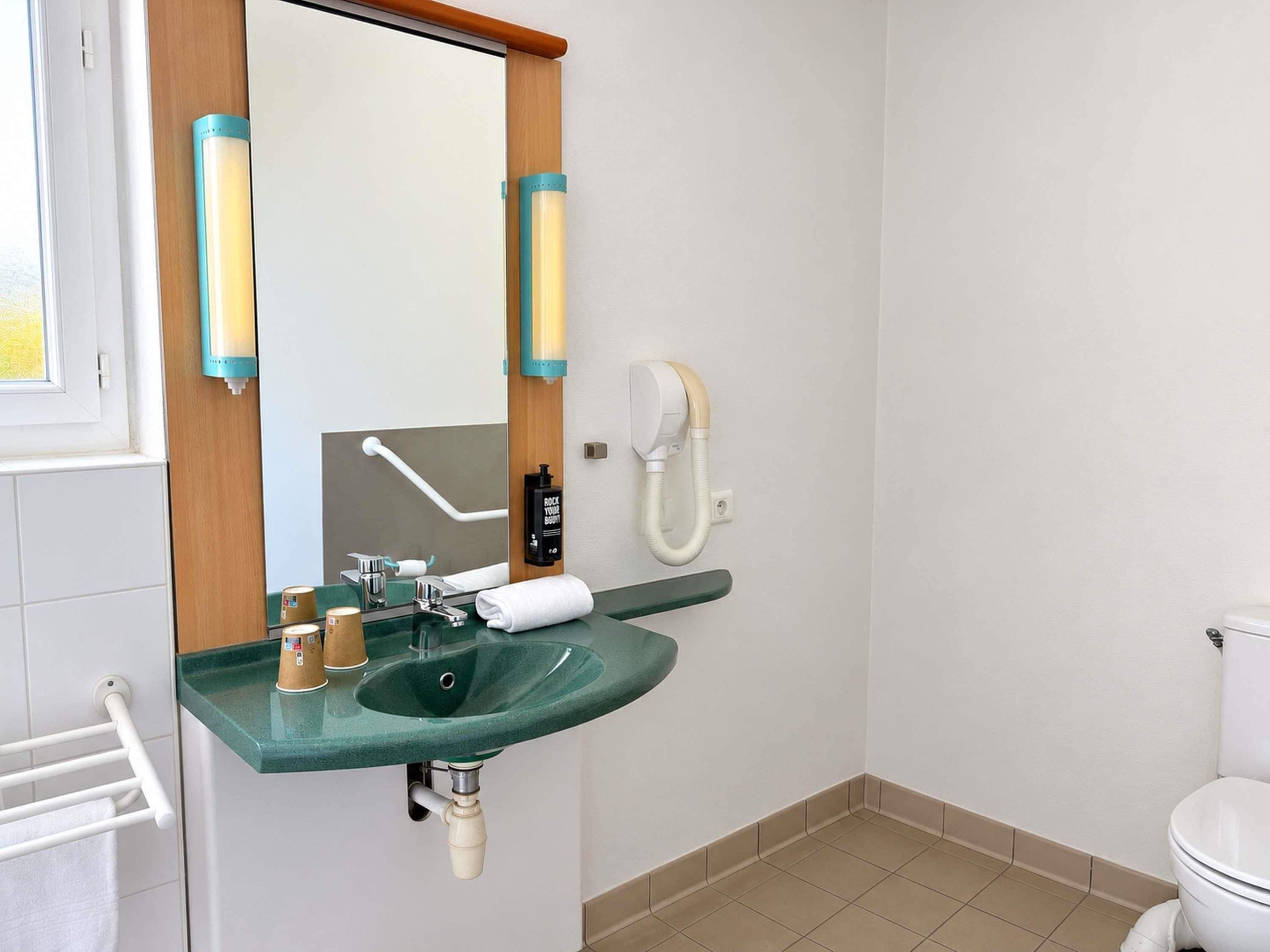 Un baño con un lavamanos verde, un inodoro blanco y un espejo con marco de madera y dos luces empotradas.